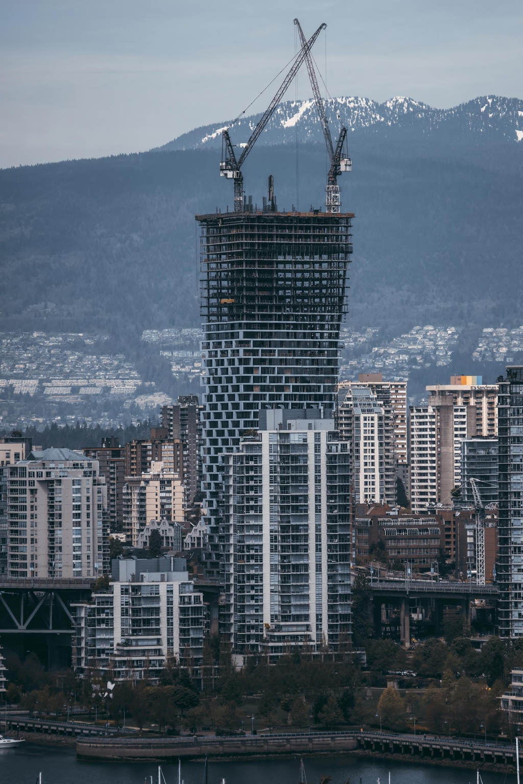 Vancouver House under construction, showcasing its twisting design and innovative architecture against the backdrop of the North Shore Mountains.