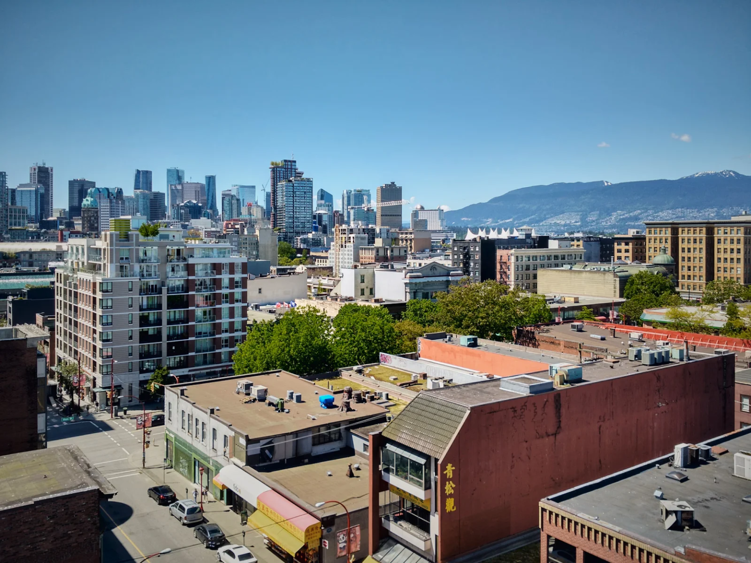 View of Vancouver's downtown skyline from Chinatown, showcasing a mix of modern high-rises and historic buildings under a clear blue sky.