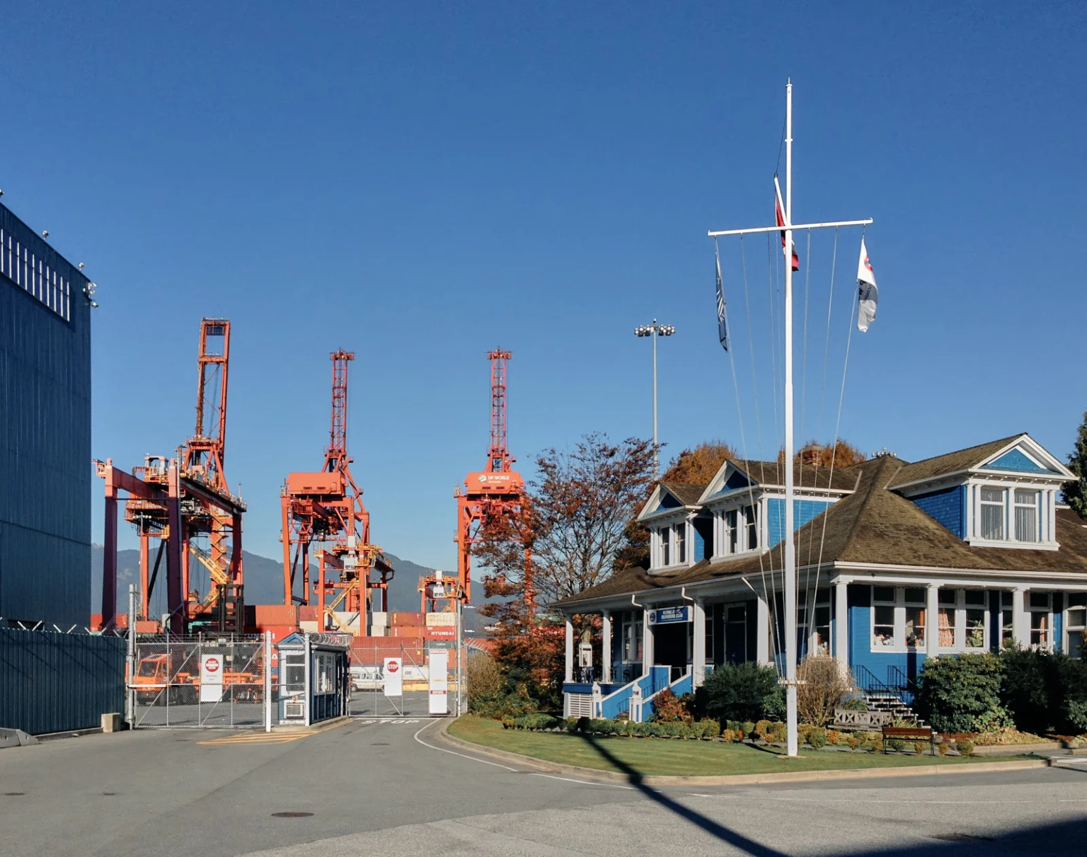 The Mission to Seafarers building in Vancouver, a historic blue-painted wood-frame structure from 1905, with modern port cranes in the background.