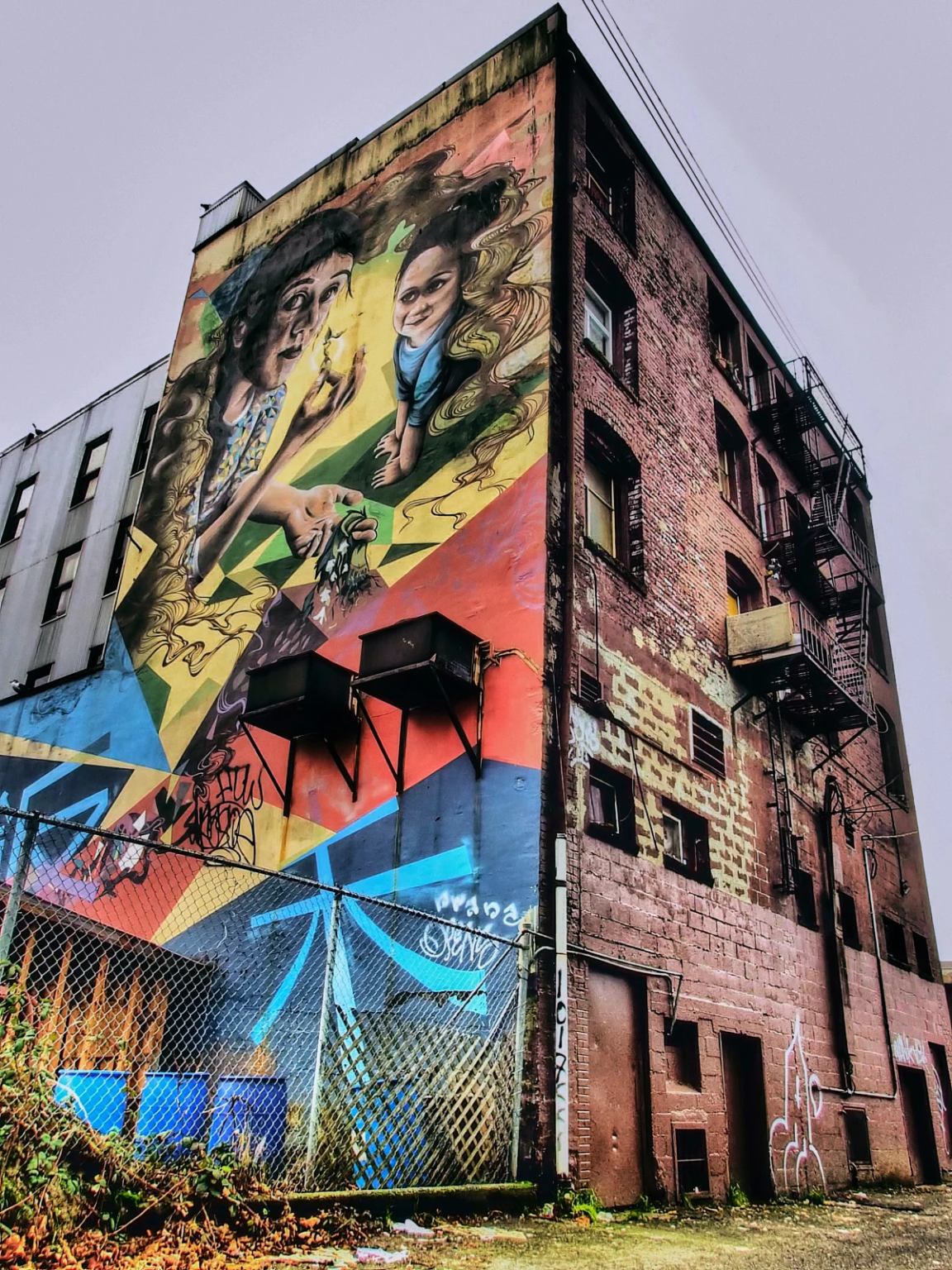 Soul Gardens mural on the Astoria Hotel in Vancouver's Downtown Eastside, featuring vibrant imagery of a woman, child, and salmon, with graffiti in the Squamish language.