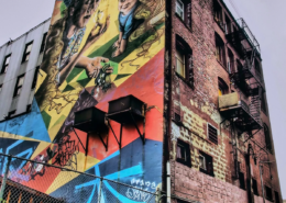 Soul Gardens mural on the Astoria Hotel in Vancouver's Downtown Eastside, featuring vibrant imagery of a woman, child, and salmon, with graffiti in the Squamish language.