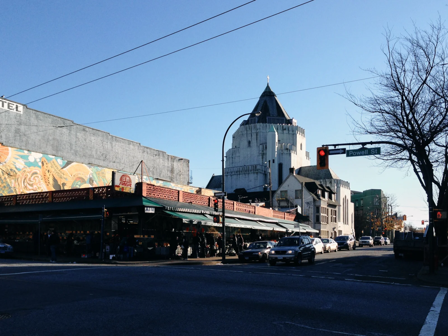 Sunrise Market on Powell Street in Vancouver, a historic community hub with a mural on the side wall, and cars at the intersection.